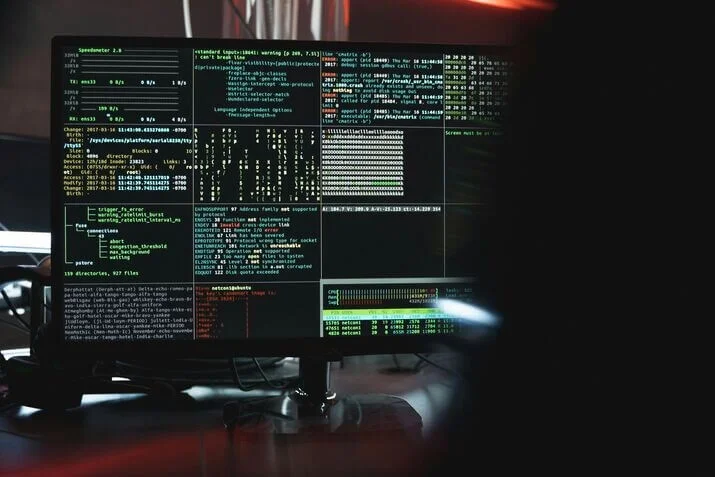 Penetration Testing 1 A computer monitor displaying multiple windows of complex code and data carrying out penetration testing. The screen shows lines of text, graphs, and various system information related to cybersecurity, indicating intensive computational or programming activities. The background is dimly lit, emphasizing the screen content.