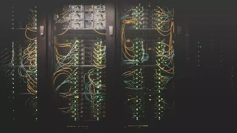 Network Security 1 A dimly lit server room with several server racks filled with network cables and hardware components. The servers are active, indicated by green and amber LED lights. The cables are organized and connected to different ports, reflecting a tidy network setup that ensures robust network security.