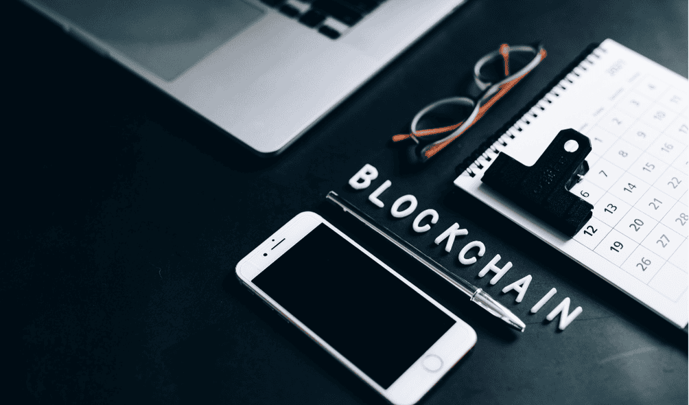 Blockchain and Cyber Security: What You Need to Know 2 Image showing a mobile phone, calendar and glasses with the text blockchain showed centered for blog post about blockchain and cyber security.
